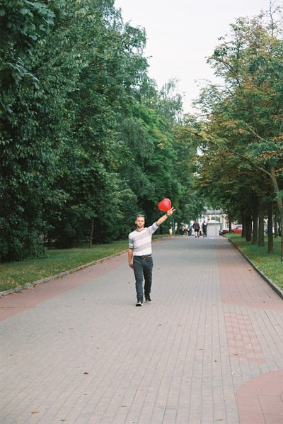 人在白衬衫和黑裤子红球在白天走在人行道上
